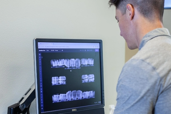 A healthcare professional examines a patient’s neck, wearing gloves, in a clinical setting. The patient is in a light blue shirt.