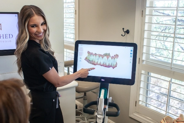 A close-up of a person inserting a clear dental aligner over straight, white teeth, showcasing neat, manicured nails.