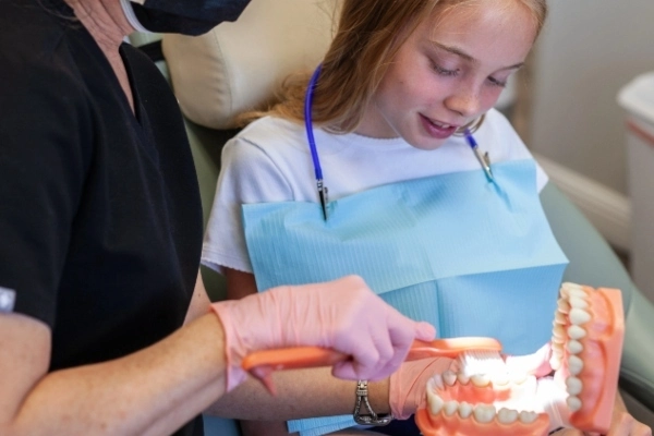 A dentist in gloves is using a dental tool while a patient reclines in a dental chair, surrounded by dental equipment.